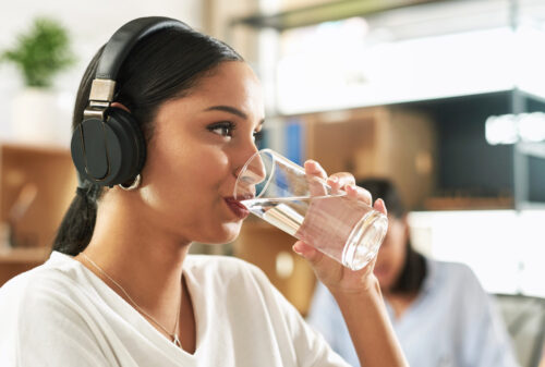 A young women wearing headphones drinking a glass of water