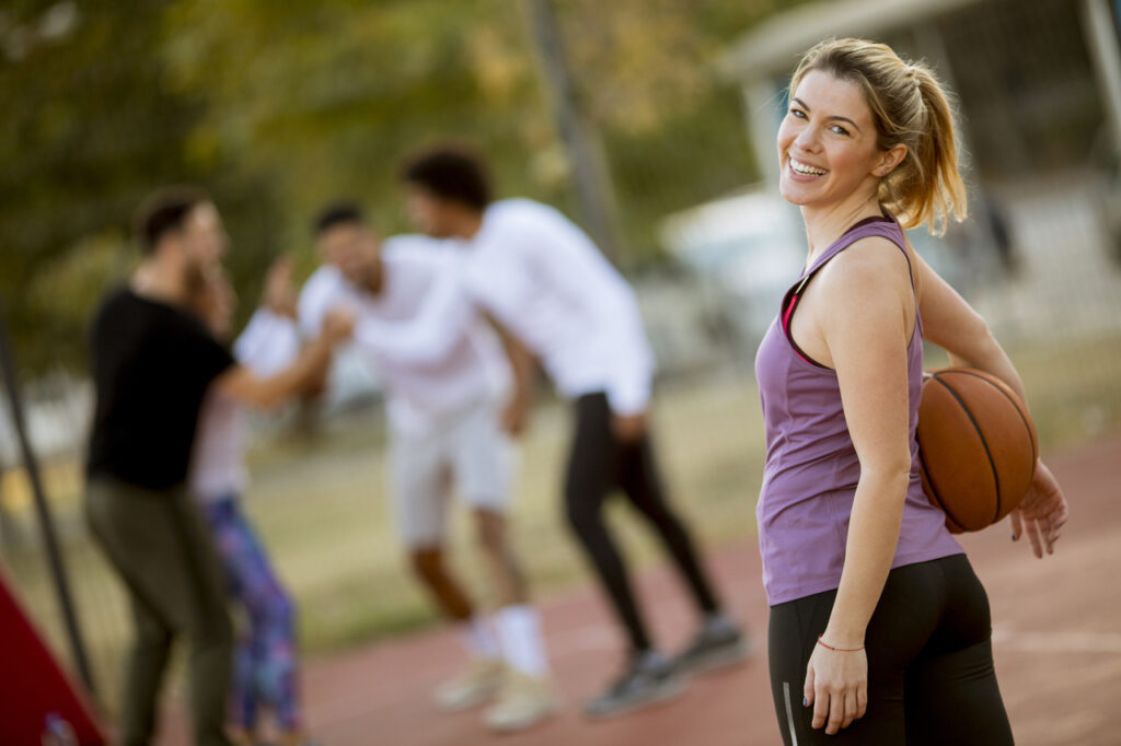 Young woman holding a basketball in an outdoors court with friends